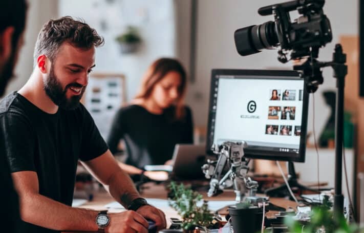 
Voici une proposition basée sur l'image décrite :

Texte alternatif
Un tournage de film corporate en entreprise, avec un salarié souriant en train de travailler devant une caméra, tandis qu'une collègue est concentrée sur son ordinateur en arrière-plan. L’écran affiche des images du projet en cours.